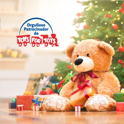 Osito de peluche sentado con regalos de Navidad debajo de un árbol, junto al texto de Proud Sponsor of Toys for Tots.